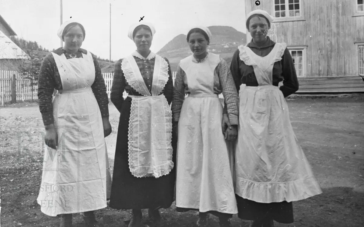4 damer i forkle står på tunet på Augedal hvor Vestoppland Folkehøgskule holdt til i begynnelsen, husholdningskurs.