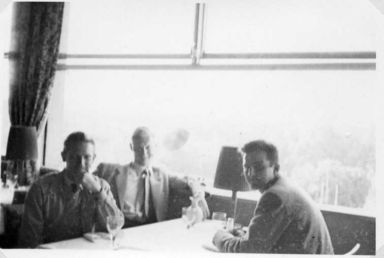 Tre män sitter vid ett bord i en restaurang med ofyllda vinglas framför sig.