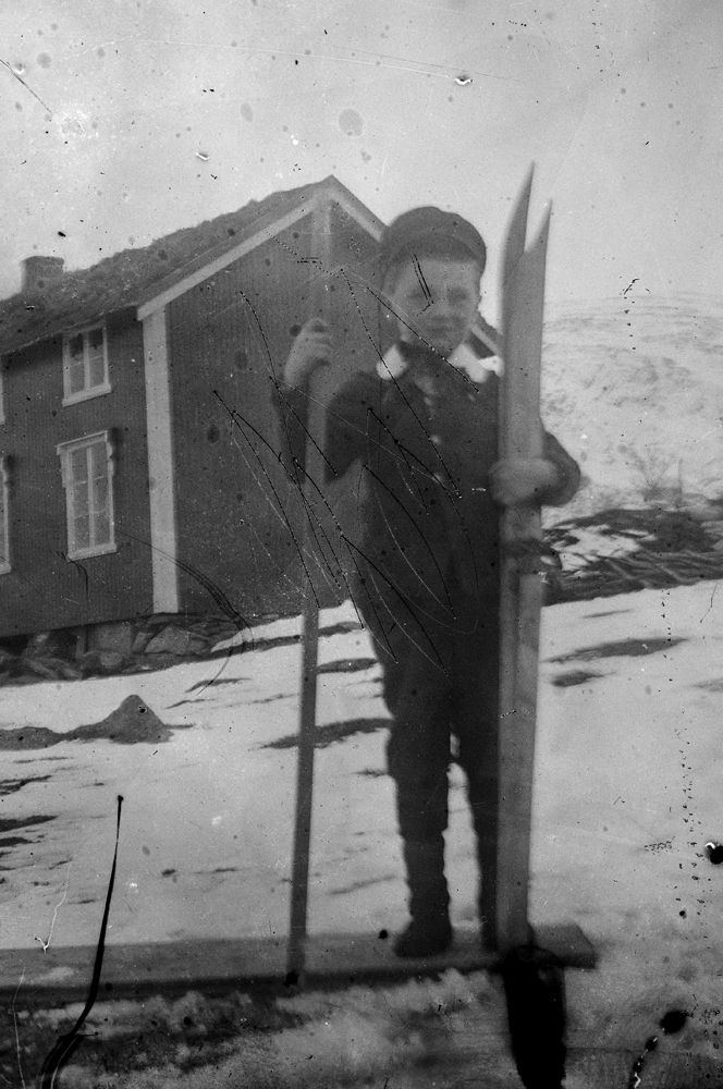 Leirfjord. Liten gutt med ski og en stav foran et hus. Gutten står på en plate og det er snø på bakken. 
Det samme huset er avbildet på LEF.F.1279