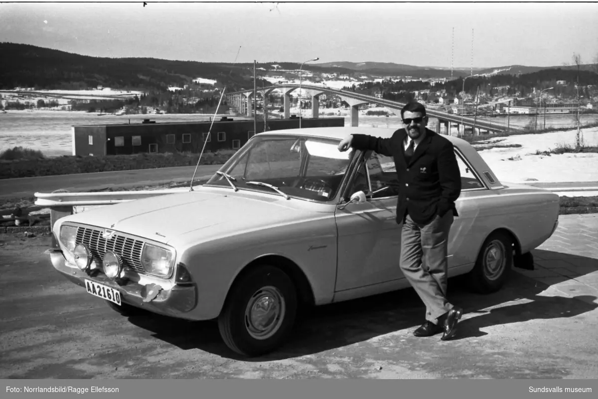 Stig Nahlbom, journalist på Expressen, poserar invid en Ford Taunus på Alnö. I bakgrunden Alnöbron och radiomasterna i Ljusta.