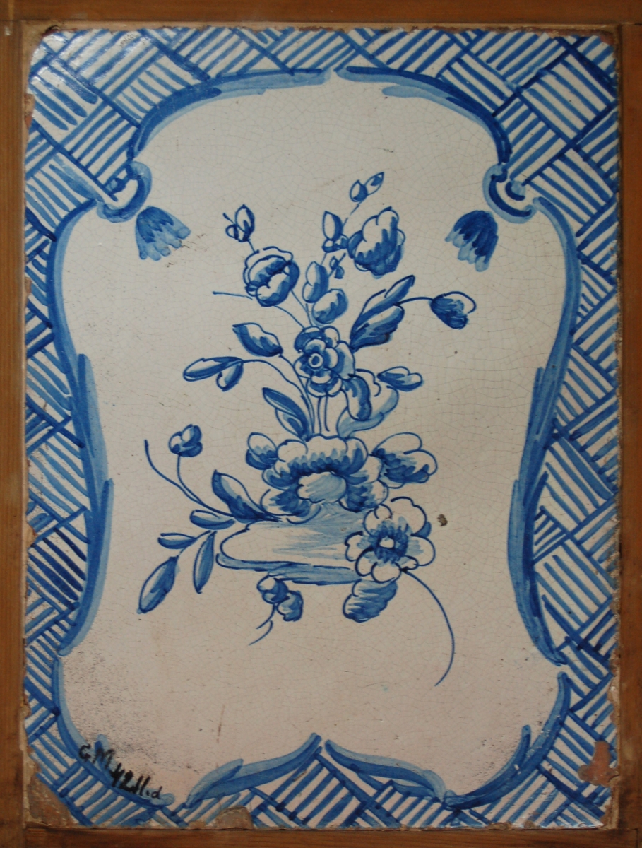 Kakelugnsplatta med blommor i rokomässig ram. Målat med blå färg.