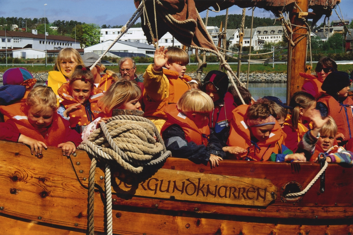 Motiv av ei gruppe barn ombord i Borgundknarren ved Sunnmøre Museum. I baksgrunnen ses Nørve skole.