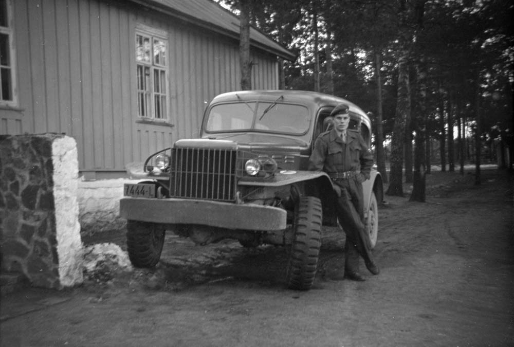 Per Kristian Skog lener seg mot en bil. Skog og bygning bak.
Bilen er en stabsvogn av typen Dodge WC 53 Carryall.