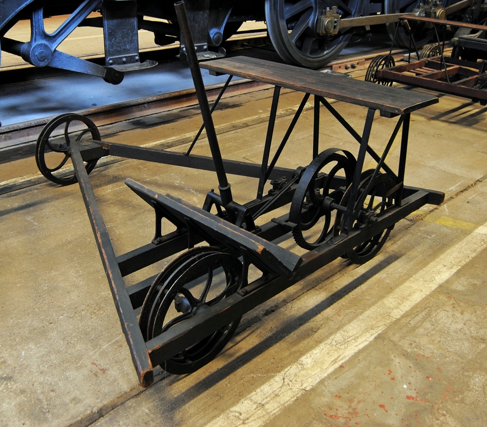 Omålad dragstångsdressin av trä avsedd för en person. Trehjuling.
Dragstång med kuggväxel, och hjul av plattjärn med gjutna nav. Spårvidd 1435 mm.