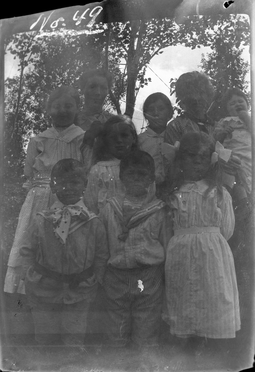 Gruppeportrett av tre kvinner og seks barn, fotografert utendørs.