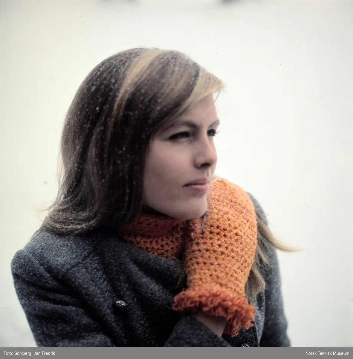 Kvinnelig modell viser vintermote. Hun har heklede votter av oransje garn.