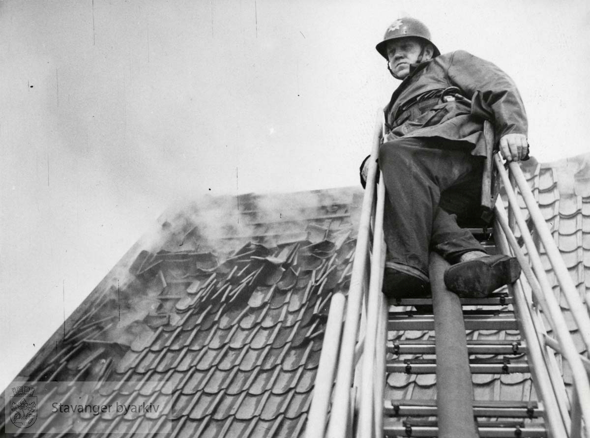 Brannmann M. Samuelsen ytterst på stige oppå taket til sjøhuset til D.S.D.