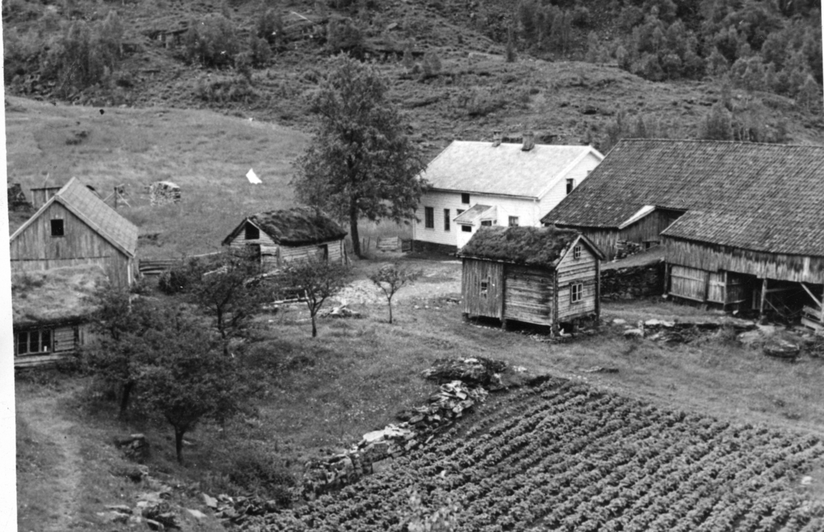 Gården Vallskår langs Hylsfjordens sørside. Det er flere bygninger på gården og dyrka mark i forgrunnen. I bakgrunnen er det beitemark.