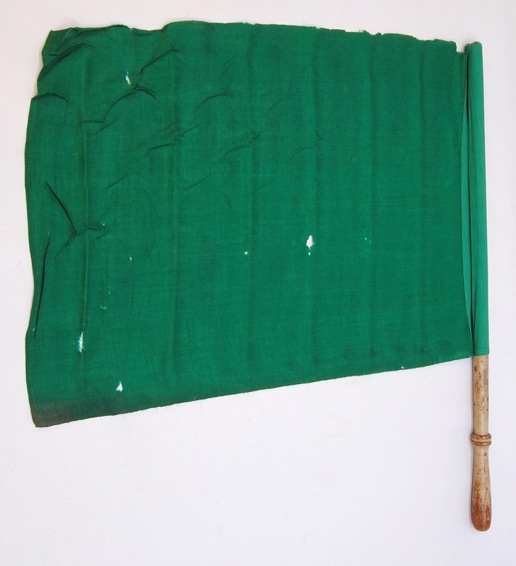 Fodral (:3) med en grön signalflagga med skaft (:1), samt endast ett skaft (:2). Skaftet (:2) ska ha en tillhörande röd flagga, men denna saknas. Det ensamma skaftet har varit rödmålat. Den gröna signalflaggan sitter fast i skaftet med två häftstift med platt huvud. Skaftet till den gröna flaggan är målad i ljusgrått. 

Fodralet är i läder och har två fack för flaggor. Det har en hållare högst upp för fastsättning i bälte eller på fordon.