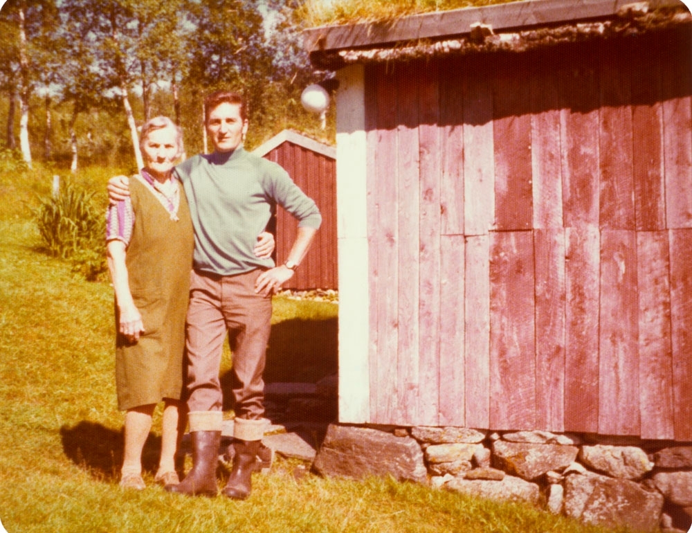 Leirfjord, Vatne, Bjønnhålo. Malla Vatne med barnebarnet Svein Johansen. Malla var født i Vatne og var siste fastboende i Bjønnhålo. Huset på bildet er bolighuset i Bjønnhålo (bislaget). Huset bak er uthuset.