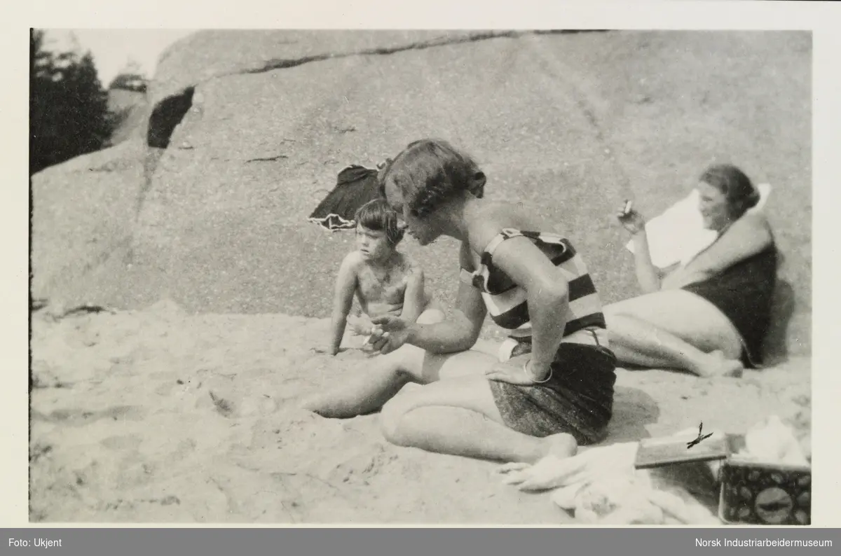 Kvinner og barn i sommerklær sitter på strand