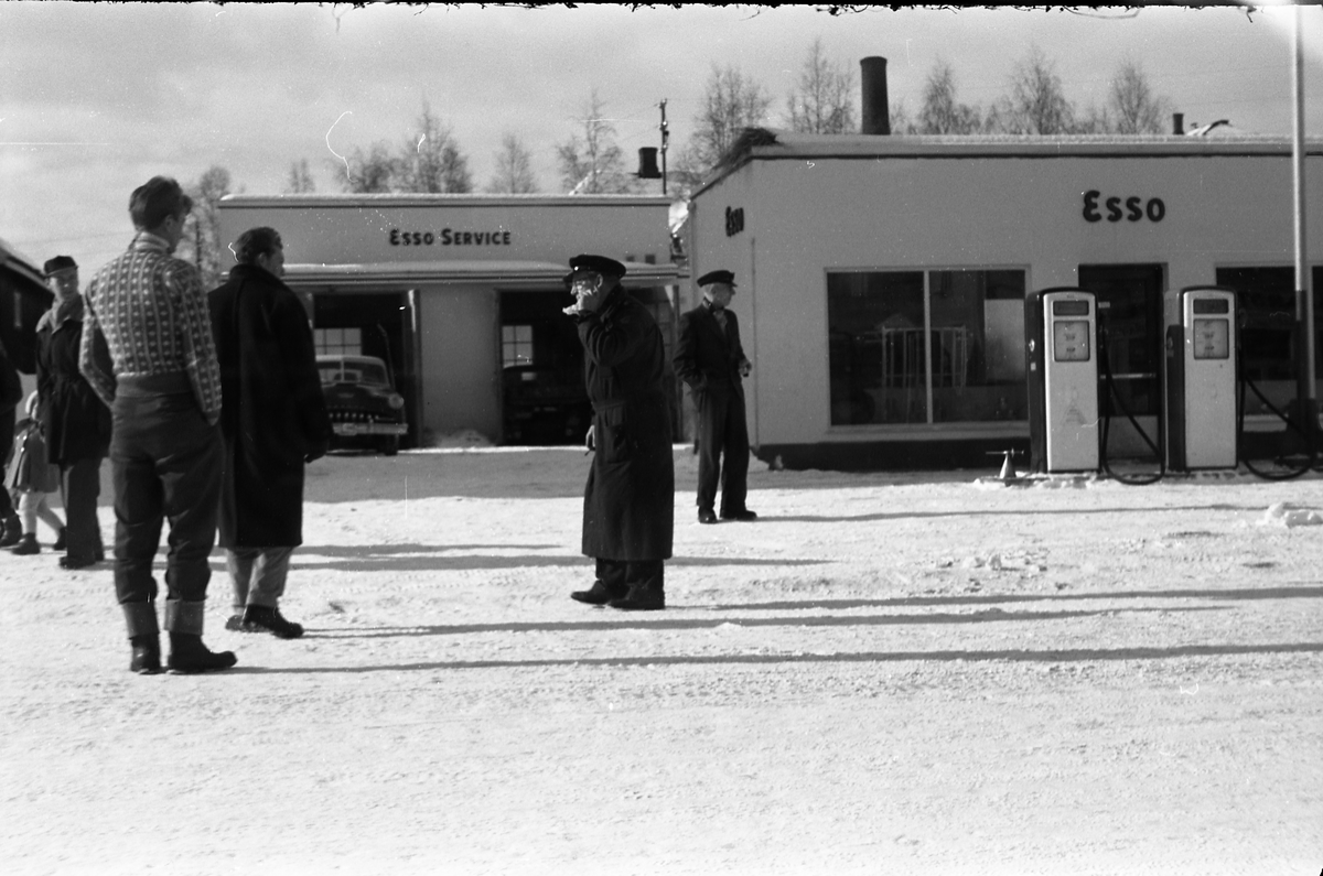 Tre bilder av noen mannfolk ved Esso benstinstasjonen på Lena februar 1958. Helt til høyre på alle tre bildene er muligens Torbrjørn Lundsten, drosjesjåfør fra Kraby, og til høyre for han muligens Paul Grindvoll.
Bilen i bakgrunnen er iflg. informant en drosjeregistrert De Soto årsm. 1951-53.