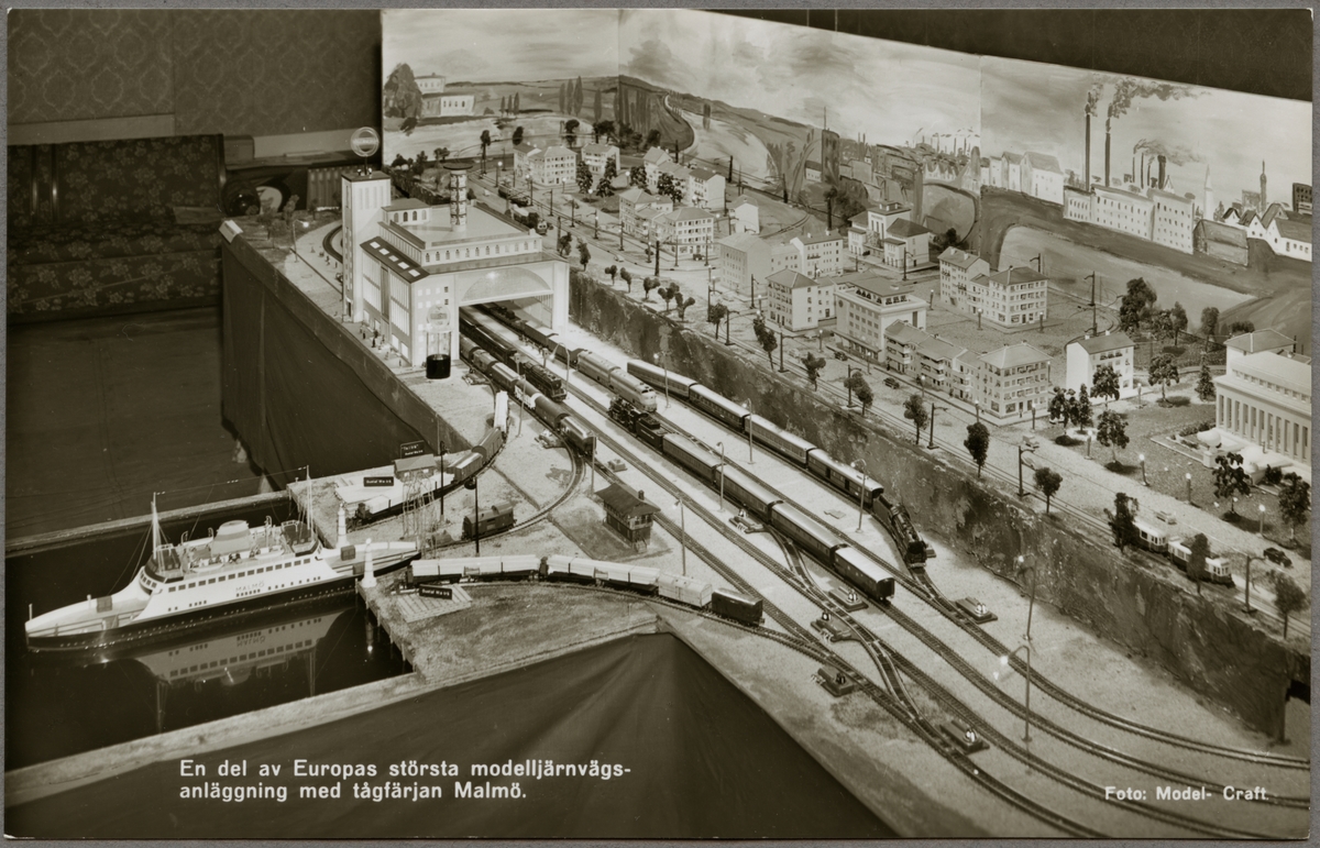 Vykort som visar en elektrisk modelljärnväg med illustrerad bakgrund.