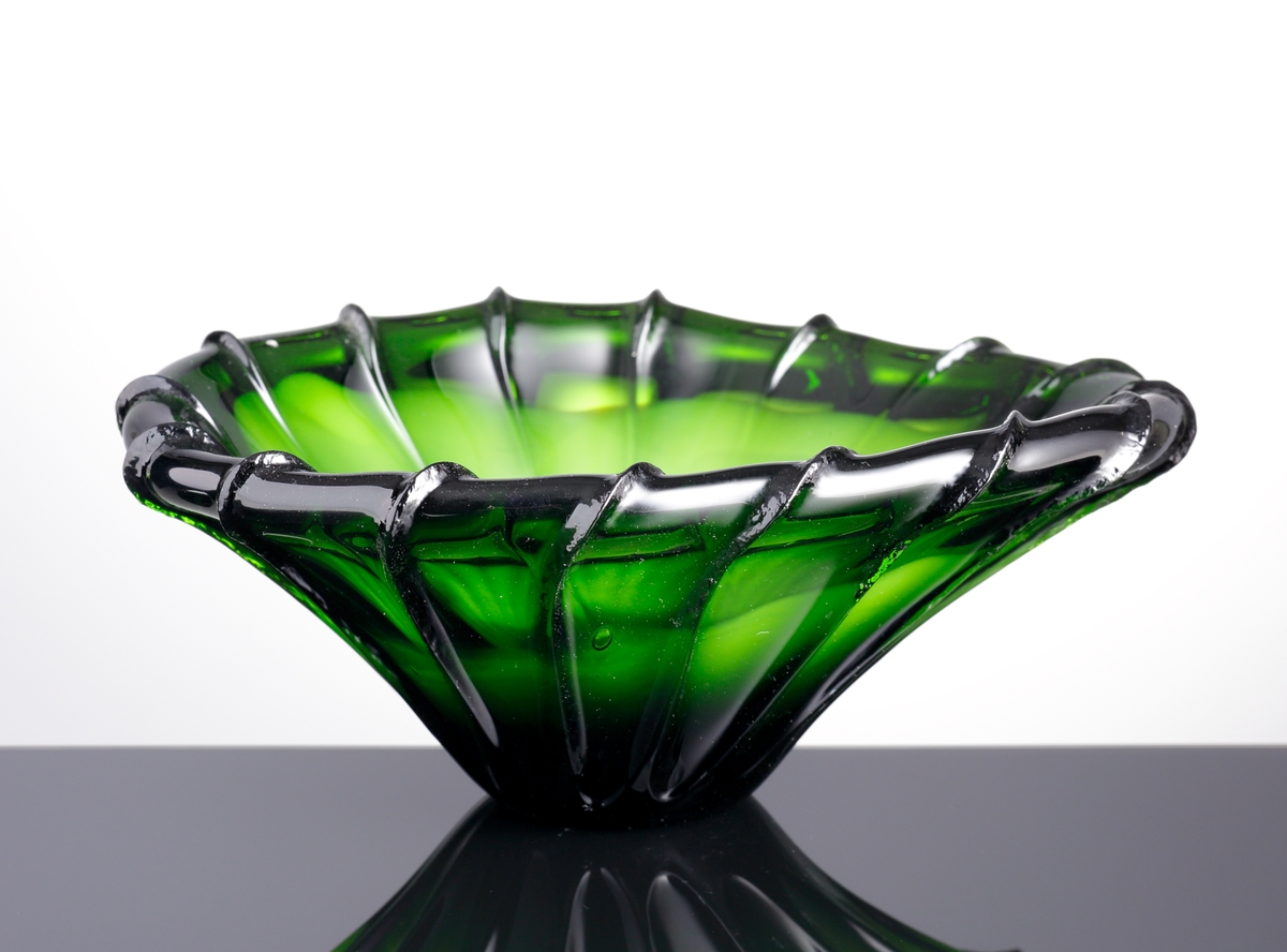 Asymmetriskt skål i grönt och vitt glas. Skålen är kraftigt räfflad.