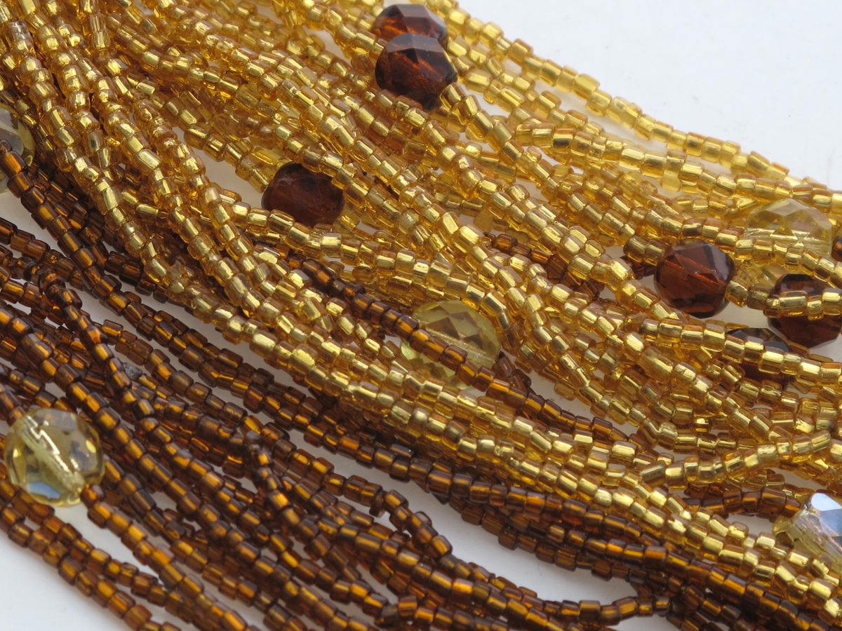 Perlekjede av brune og gule perler, tredd på 46 lenker, fordelt i 4 "bunter", festet til et metallbeslag, som igjen har montert et kort kjede med, krok og øye.