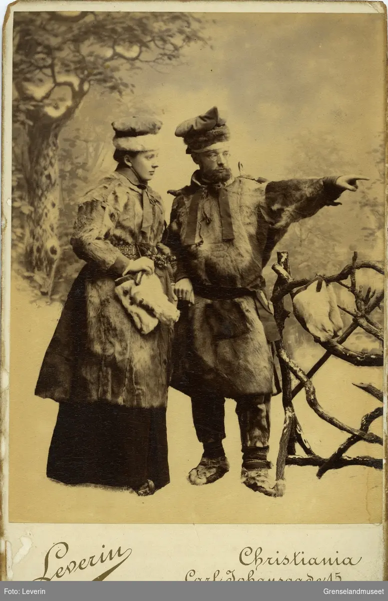 Studiefotografi av Distriktslege Andreas Bredal Wessel og hans kone Ellisif Wessel ikledd pesk, skaller og stjernelue foran et tregjerde.