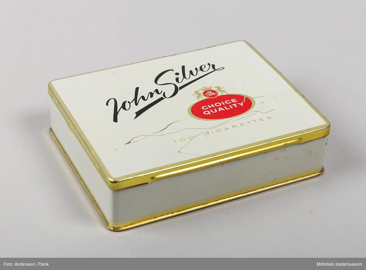 Plåtask John Silver som har innehållit 100 cigaretter tillverkad av AB Svenska Tobaksmonopolet, troligtvis från 1950-talet.

John Silver är ett svenskt tobaksmärke som lanserades efter andra världskriget för att att konkurrera ut de amerikanska tobaksmärken som blivit populära vid samma tidpunkt. Märket har fått sitt namn av piraten Long John Silver från boken Skattkammarön. 1958 blev John Silver det största tobaksmärke som såldes i Sverige. 

Plåtasken är vit, har guldfärgade kanter och undersida. På kortsidorna finns även 
"AB SVENSKA TOBAKSMONOPOLET" inristat,  På askens ovansida finns John Silvers logga. På lockets insida står namnet: "John Silver". På undersidan av asken finns ett klistermärke med tryckt text: 
"KONTROLL - STÄMPEL - TOBAKSMONOPOLET
RIKTPRIS 16:--kr. Får enl. lag säljas endast i hel förpackning".