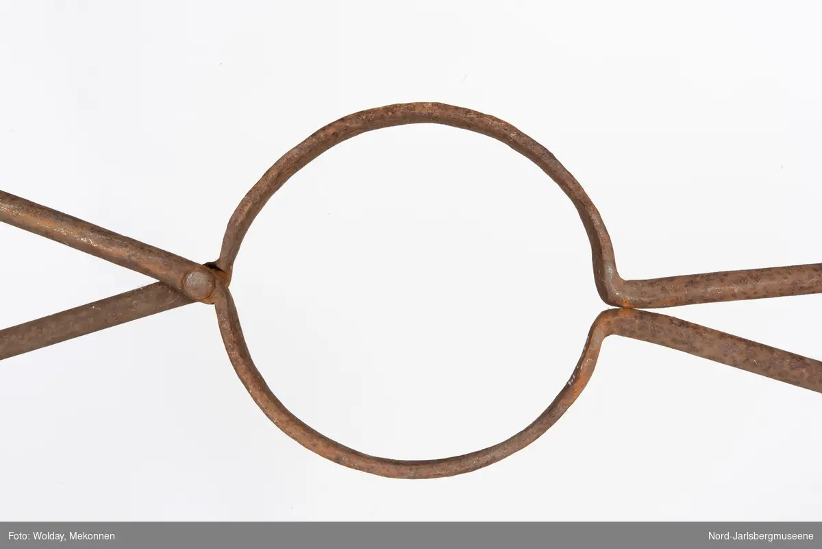 To stenger som krysser hverandre via en rund ring i midten. Den brukes slik at to menn holder  på hver sin side, og trer ringen over digelen for å løfte den opp.