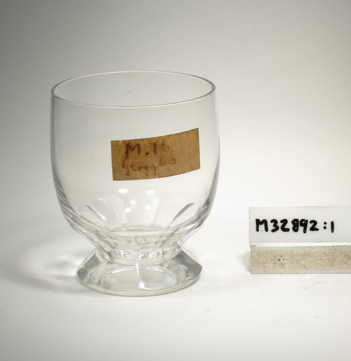 Svagt elliptisk kupa på konisk klack. Glaset är facettslipad i 9 bågar.
Lapp: "M.16 Grogglas"