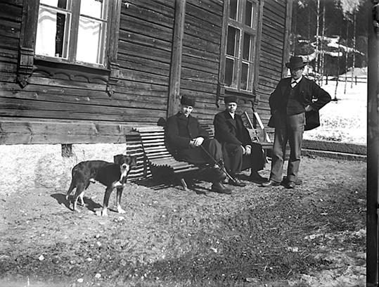 Tre män på/vid en bänk och en hund, Riddarhyttan.