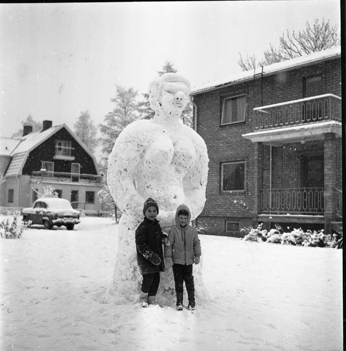 Två barn står framför en mycket hög snögubbe, eller snarare snögumma då ...