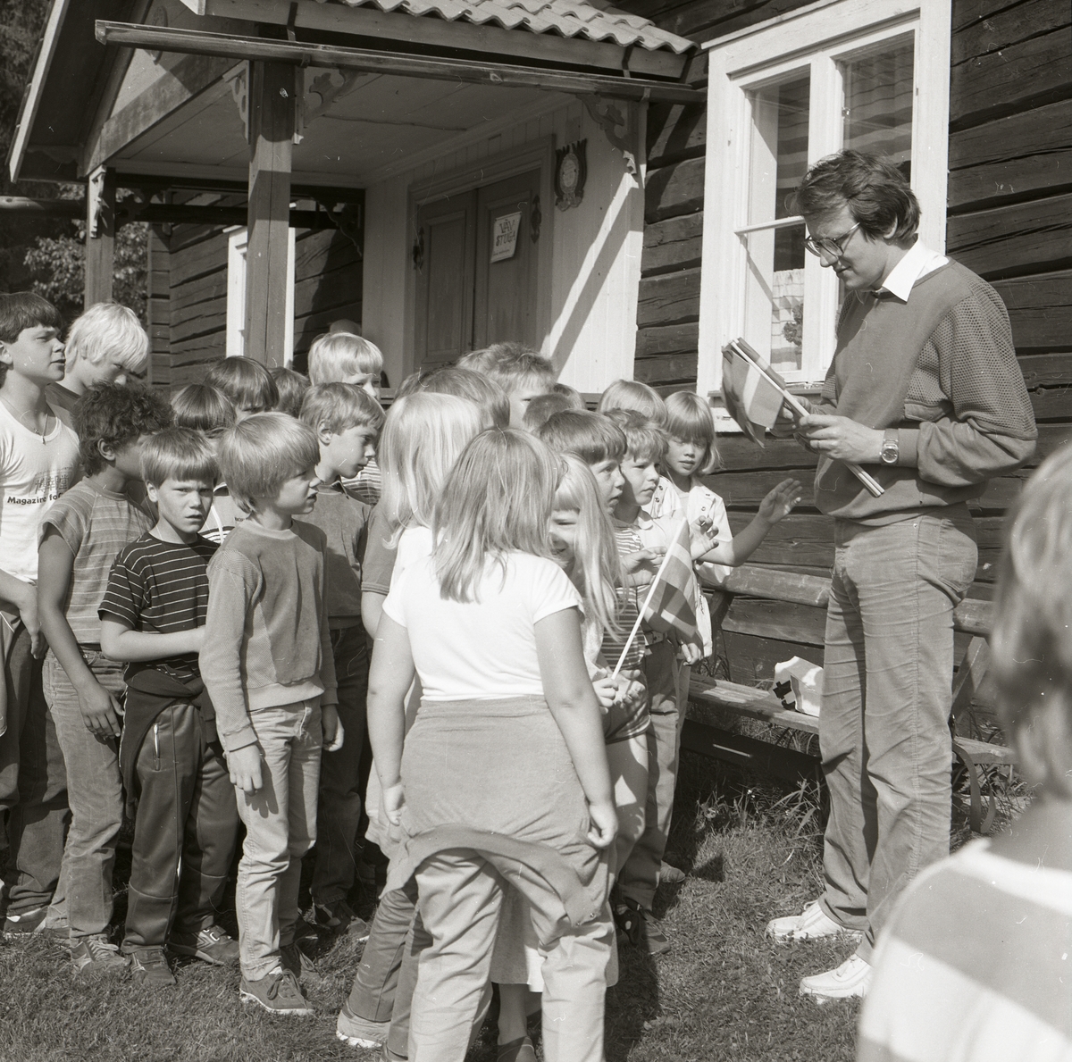 En man delar ut flaggor till en grupp barn vid nationaldagsfirande i Rengsjö hembygdsby, 6 juni 1984.