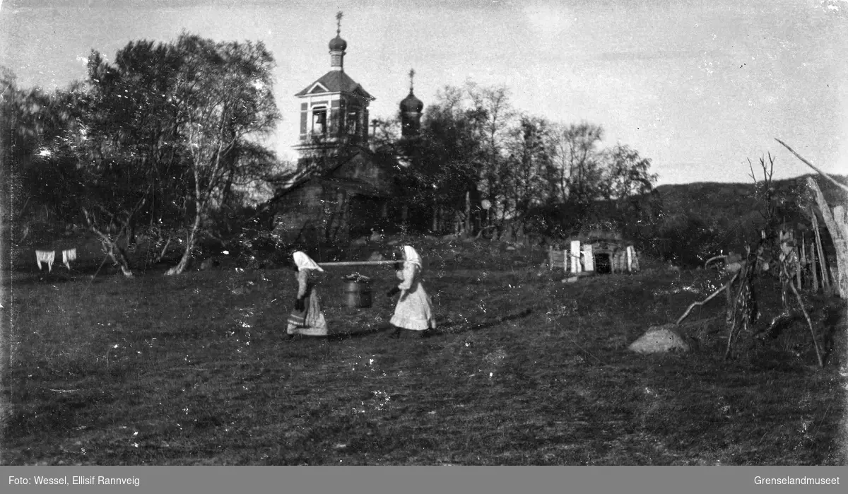 To kvinner bærer en tønne mellom seg på åk, Boris Gleb. Kirken ses bak.