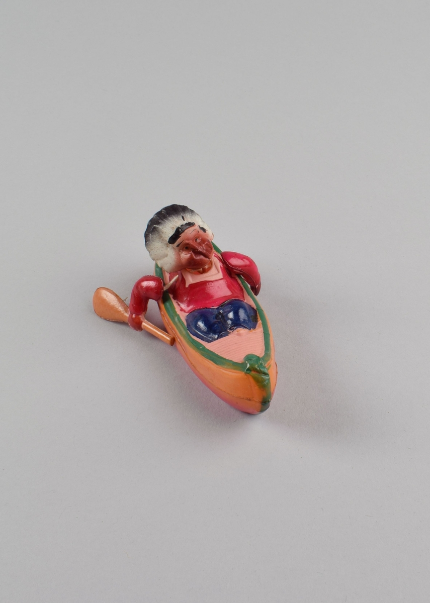 Lekefigur av indianer i kano. Bevegelige armer og hode festet med innvendig tråd.