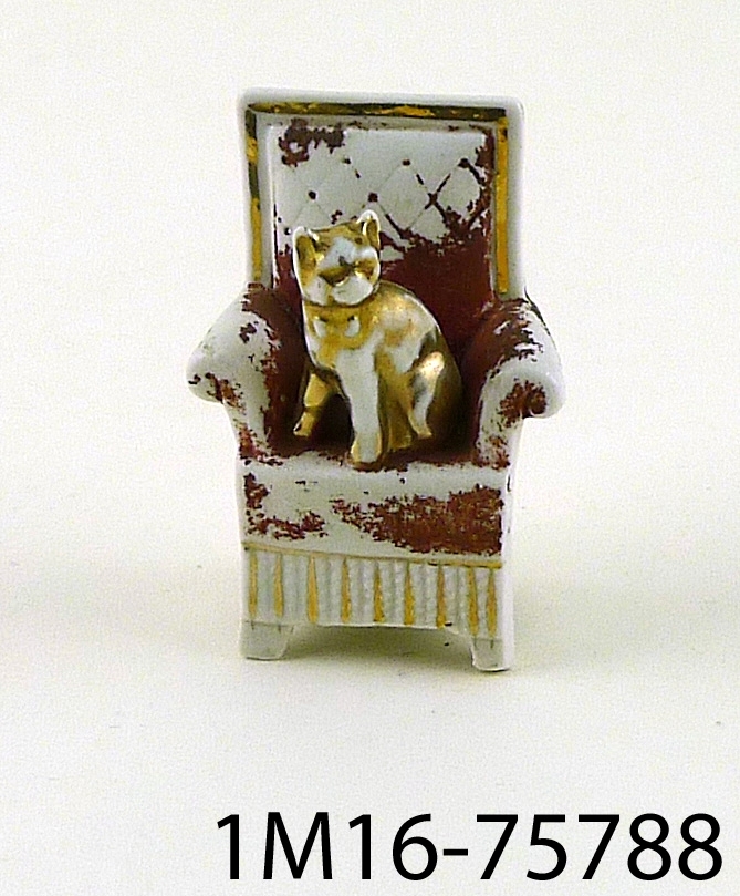 Prydnadsföremål av porslin, förgylld katt i rödklädd stol, på baksidan märkt: G.G. Germany.