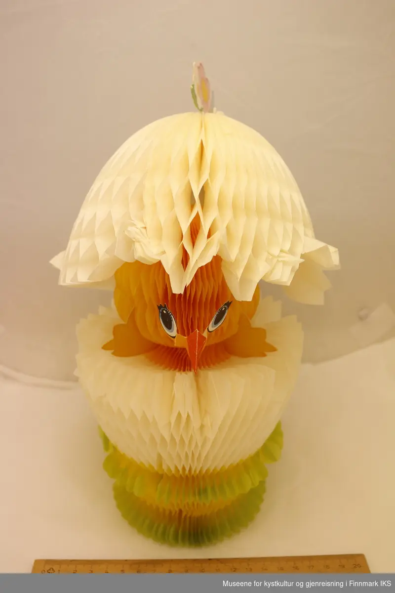 En utfoldbar papirfigur av en påskekylling i skallet sitt. Skallet kan foldes over hodet på kyllingen, og festes på plass ved bruk av binders. Hele figuren kan foldes flat