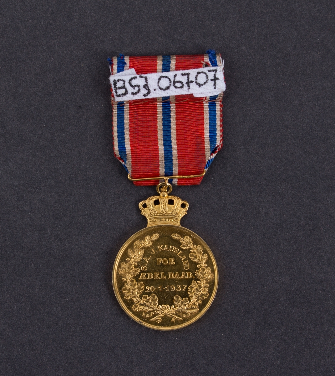 Gullmedalje gitt til Simon Kausland på MS VENUS for sin innsats under redningsaksjonen av besetningen på DS TRYM den 20. januar 1937. Kong Haakon VII gullmedalje med krone med bånd og jakkefeste.