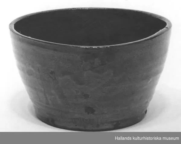 Skålen är av bränd keramik. Brun-svart färg, glaserad. Märkt i botten "Cederholm, Varberg."