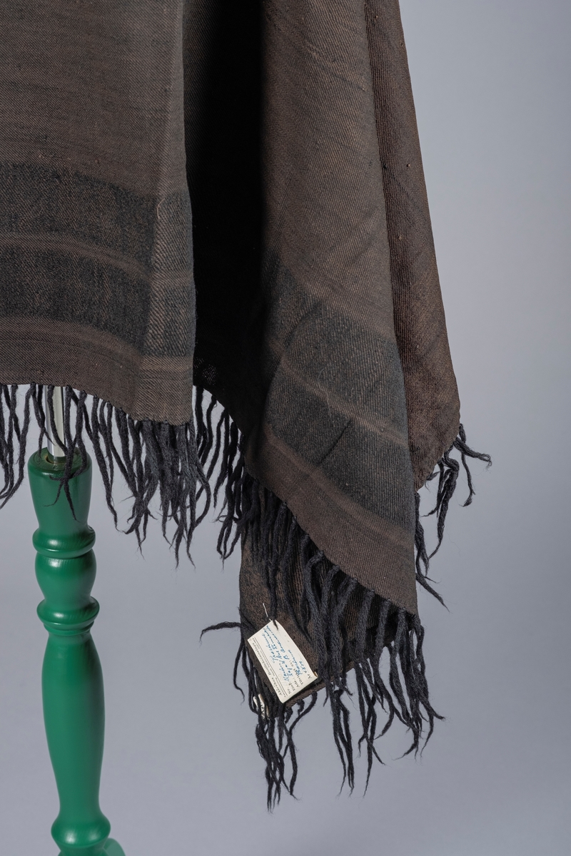 Sort sjal sydd sammen av to deler. Det er frynser i kantene. Sjalet har mønster av to brede striper langs kantene.
