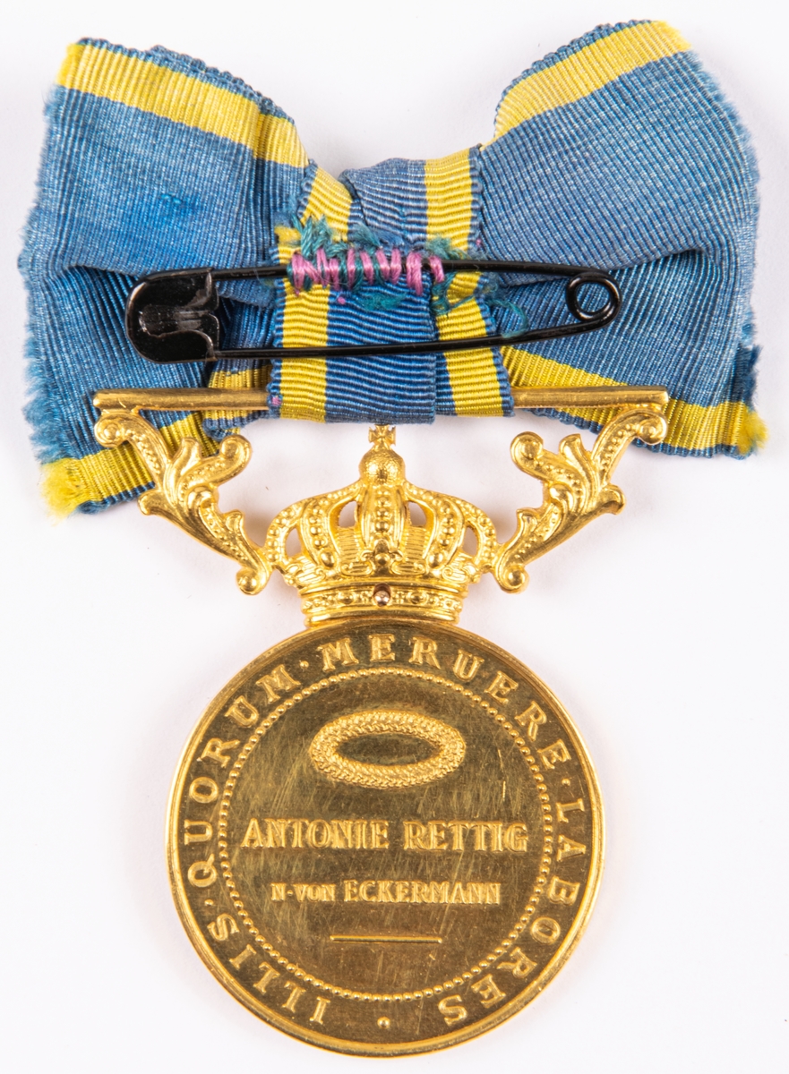 Medalj.
Guld, av A. Lindberg.
Konsulinnan Antonie Rettigs Illis Quorum, diam 3,2cm.
På ena sidan Gustav V i reliefprofil från vänster. På den andra sidan "Antonie Rettig. N. von Eckerman".
Vid ovankanten krona samt blågult band.
