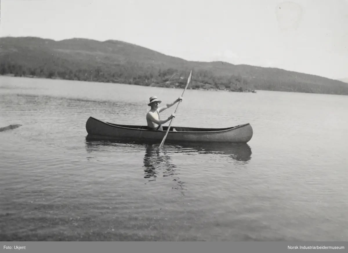 Mann med hatt sitter i kano og padler