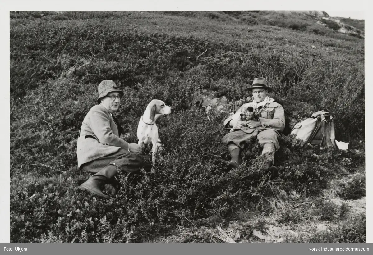 James Coward og mann sittende i lyngen i fjellet med to hunder