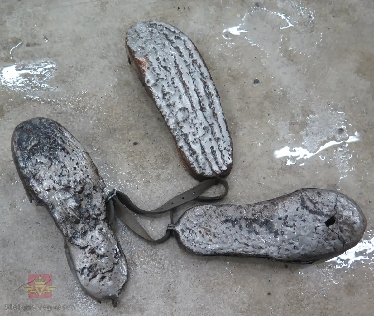 Slepesko av metall, forsterket med slitelag på undersiden. To av skoene henger sammen med ei lærreim.