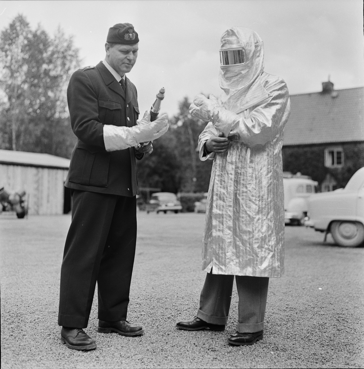 Brandkåren - en man i skyddskläder och en man i uniform med brandredskap, Uppsala 1957