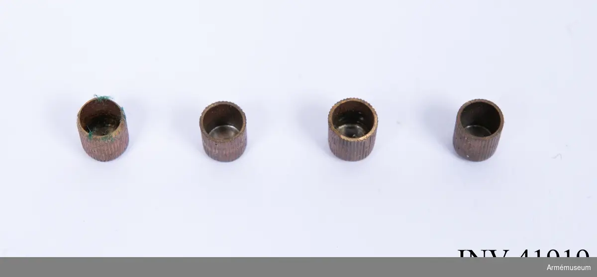 Grupp E III.
Låda med glaslock.Lådan innehåller: en kultång av mässing märkt på skänklarna med "48" och "WD", en "smörjdosa" av aluminium, fem stycken tändhattsnipplar, fyra stycken tändhattar av koppar troligen skarpa, en läskstång av trä med mässingsända, en tändhattsnippelnyckel med rensnål i handtaget, åtta stycken blykulor (korroderade), en burk i lackerad plåt med texten: "250 Eleys superior anti corrosive caps. warraned neihter to miss fire or fly to pieces. No. Made expressly for Webbleys patent safty pistols & revolvers", en plåtburk (tom) med texten: "It is essential that this Lubricating paste should be applied to all bullets before loadning." Det verkar som om lådan har varit utställd tidigare då man försökt fästa innehållet med ståltråd och limmat och spikat (!) fast plåtburkarna. Glaset i locket passar dåligt och är mycket illa tillskuret, ditsatt efteråt måhända?