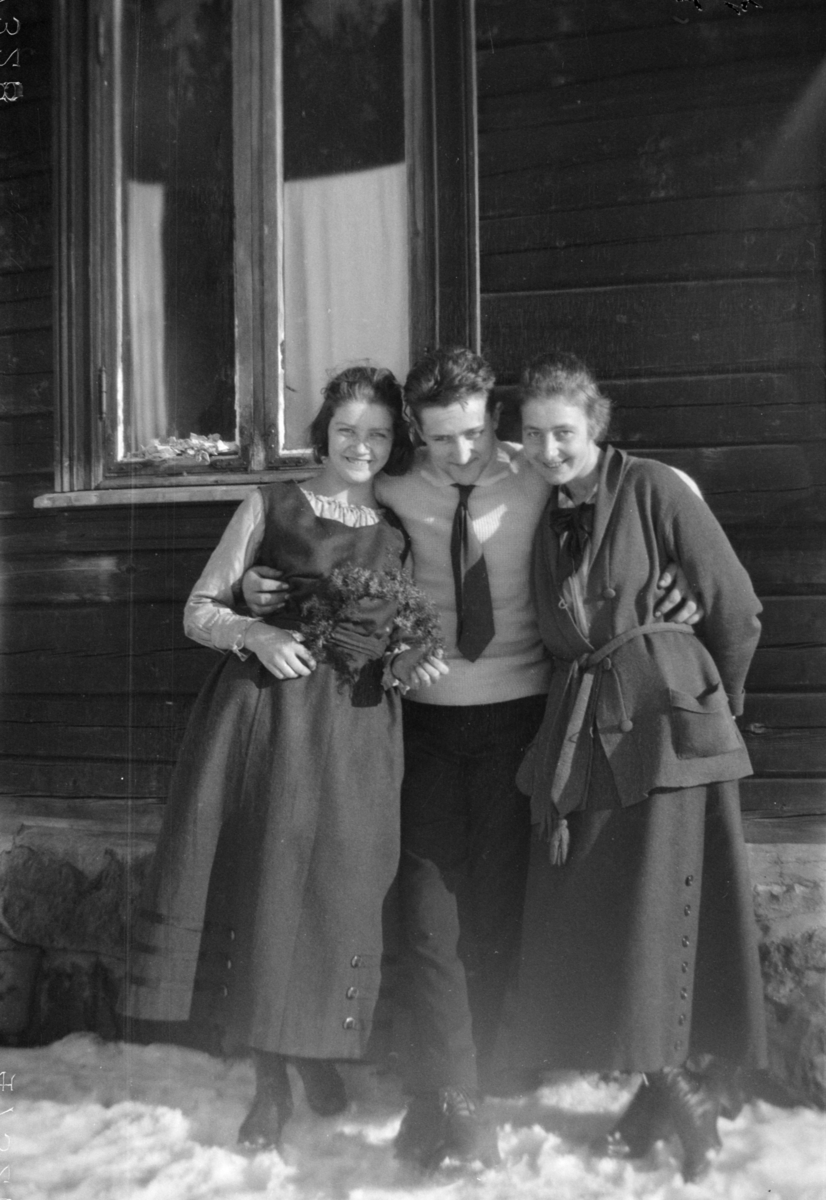 Fotografen og to unge damer, en av de med en blomsterranke i hånda. Vinterbilde.