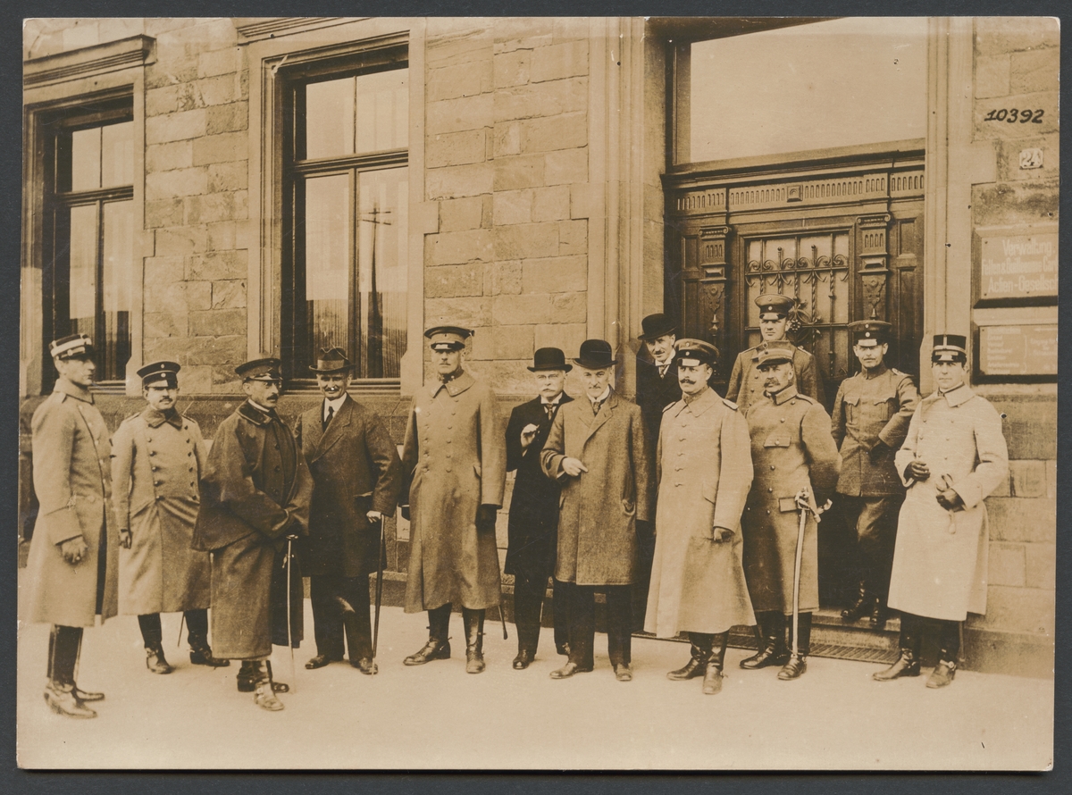 Fotografiet förställer ett grupporträtt av militärer och civila personer framför en byggnad. Skylten på höger sidan talar om att det är "Verwaltung Felten & Guilleaume Carlswerk Actien Gesellschaft".