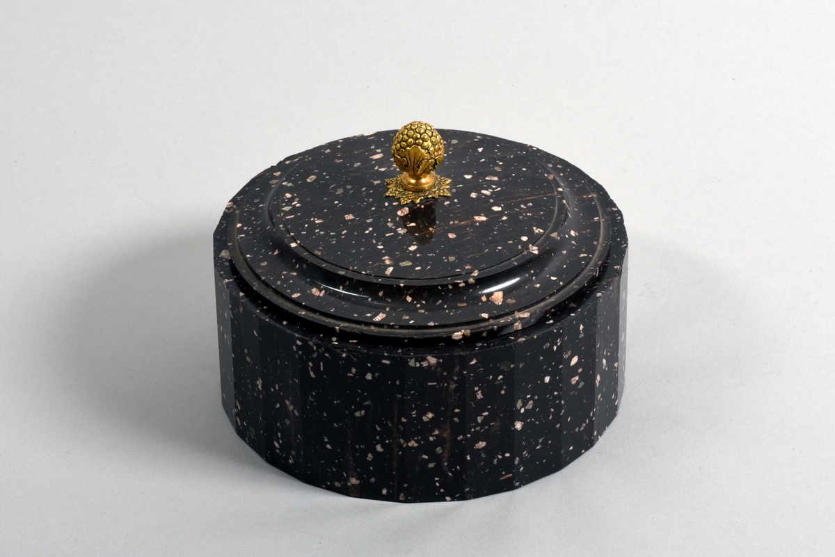 Dosa med lock av porfyr från Älvdalen. Fasettslipad dosa. Locket har en knopp i forma av en förgylld vindruvsklase av brons.