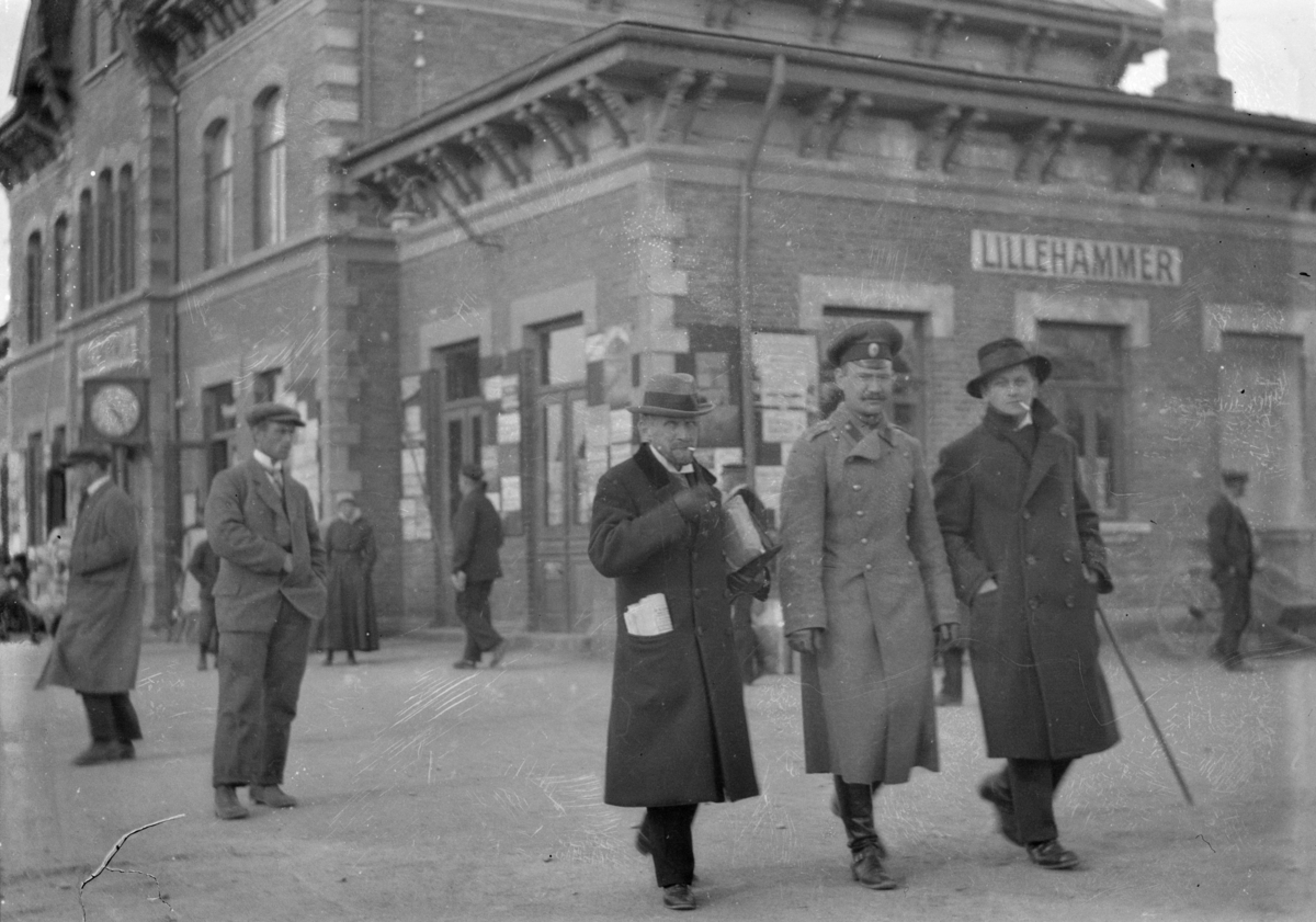 I forgrunnen tre menn, hvorav en med uniform, på Lillehammer stasjon