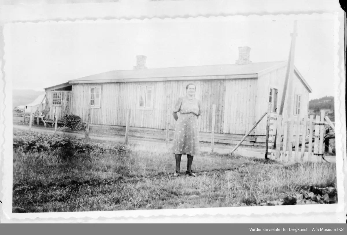 Kvinne står foran et bolighus med gjerde og grind til høyere.