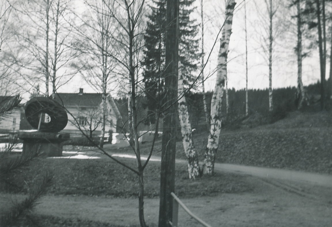 Formannsbolig og repartørbolig  på Kistefoss, og monument på sokkel, kan skimtes mellom trær på fabrikkområdet.