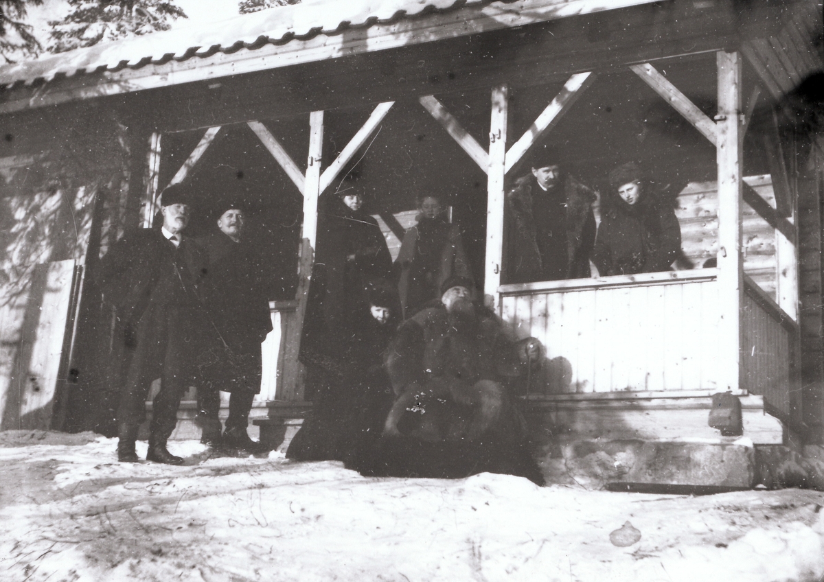 Fire vinterkledde menn, inkludert konsul Anders Sveaas, og fire kvinner på veranda til Mosjøhytta.