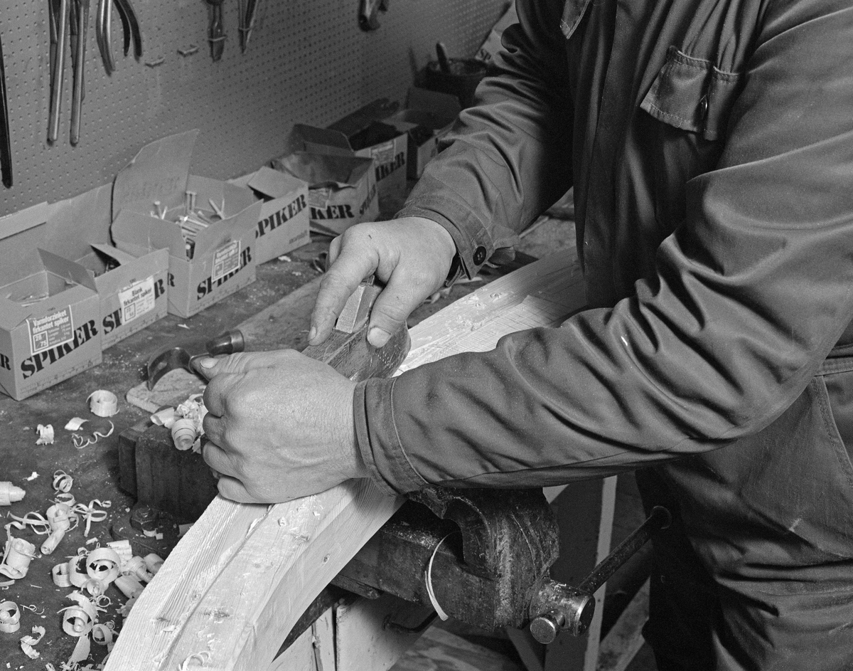 Fra Glomma fellesfløtingsforenings båtbyggerverksted på Flisa i Åsnes kommune i Solør. Lars Bernhard Olastuen, høvling av stevn, høvler for hånd. Bygging av fløterbåt (Flisa-båt) november 1984. Arbeid med stevnene før de blir spikra fast til kjølen.