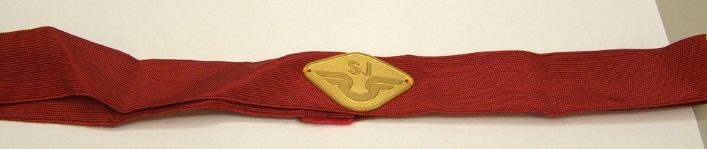 Rött vävt mössband med fastsytt guldfärgat mössmärke från 1985-1991.