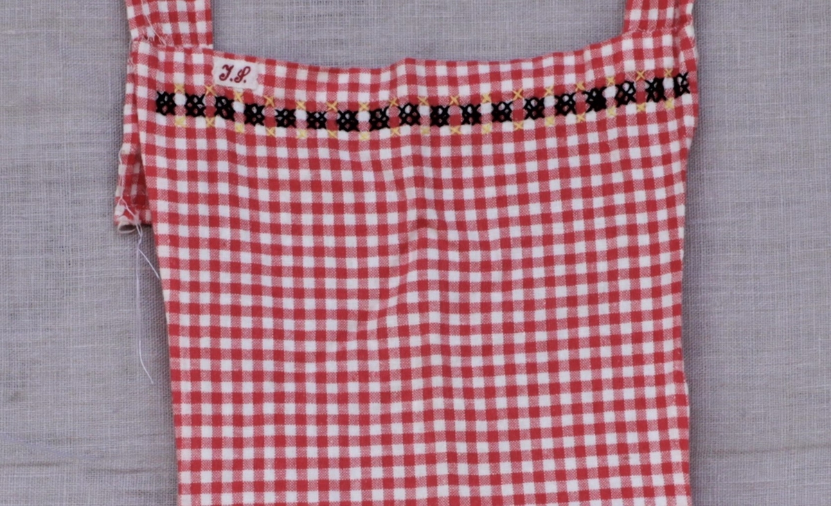 Rødrutete bomullsforkle med knytebånd og lomme. Pyntet med brodert bård øverst og på lommekanten.