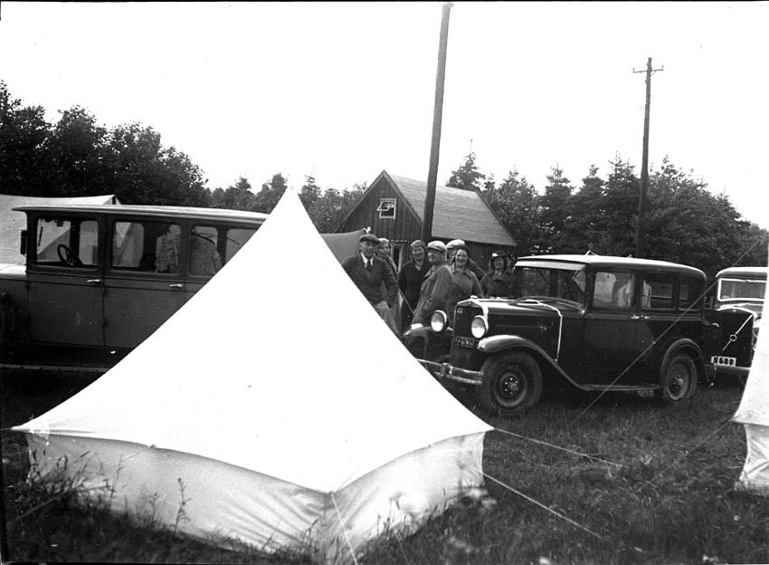 En grupp personer, tält och bilar på en camping.